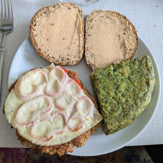 Homemade chicken burger with sweet pepper and cheese on it, potato/spinach tortilla, and homemade spelt bread with homemade red lentil hummus